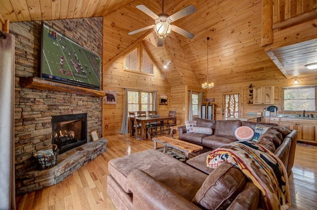 living room with light hardwood / wood-style floors, wooden walls, wood ceiling, high vaulted ceiling, and ceiling fan with notable chandelier