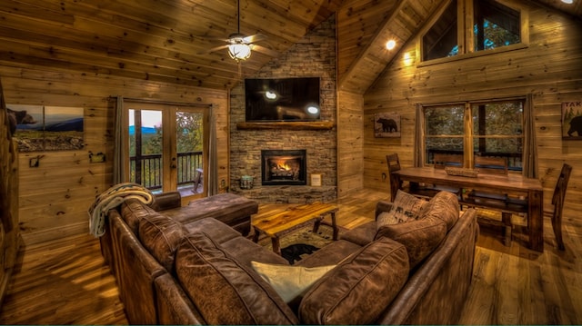 living room with ceiling fan, wood-type flooring, high vaulted ceiling, and wood walls