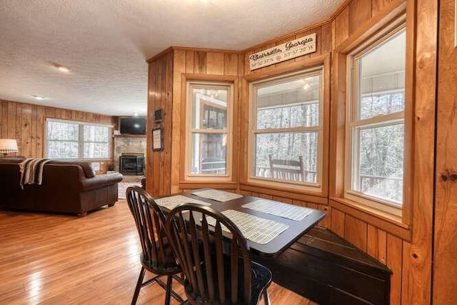 dining area with a glass covered fireplace, wooden walls, light wood-style floors, and a textured ceiling