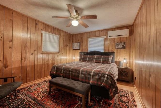 bedroom featuring a ceiling fan, wood finished floors, baseboards, wood walls, and a wall mounted air conditioner