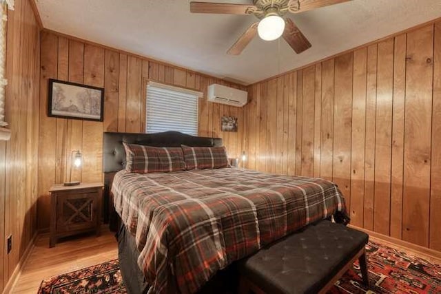 bedroom with light wood finished floors, baseboards, wood walls, a wall mounted air conditioner, and a ceiling fan