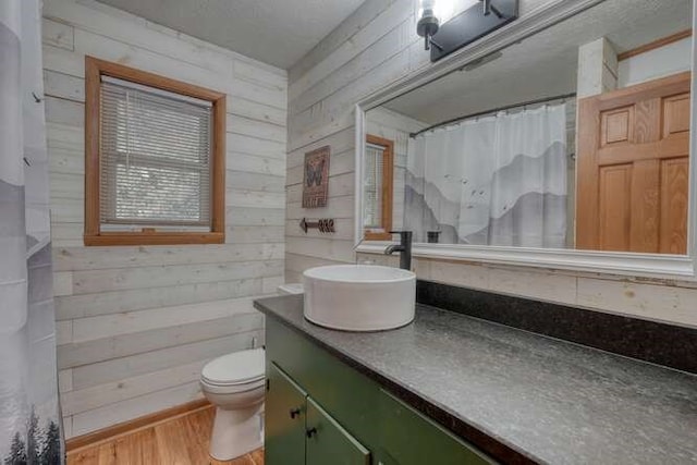 full bathroom featuring wooden walls, curtained shower, toilet, wood finished floors, and vanity