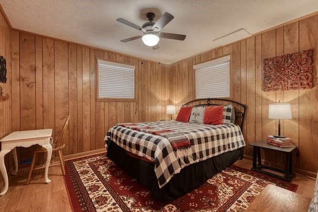 bedroom with a ceiling fan, wood finished floors, and wood walls