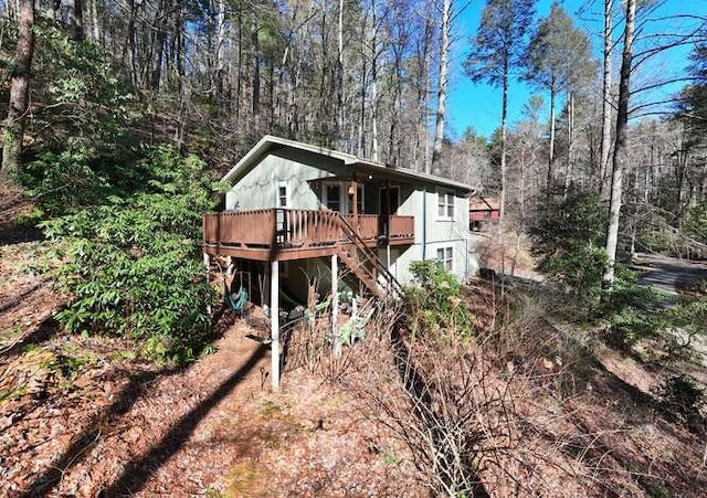 back of property with a deck, a wooded view, and stairs