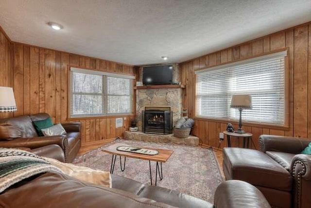 living area with a stone fireplace, wood walls, a textured ceiling, and wood finished floors