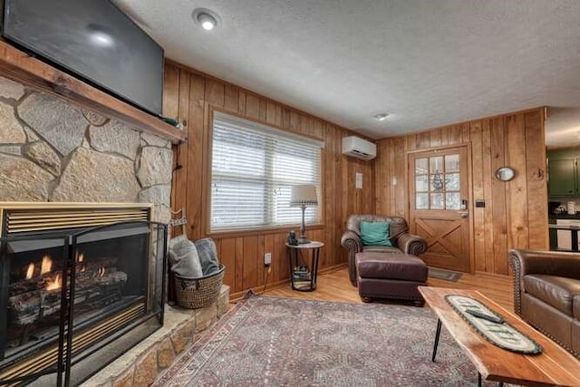 living area with wood walls, a stone fireplace, wood finished floors, a textured ceiling, and a wall mounted AC