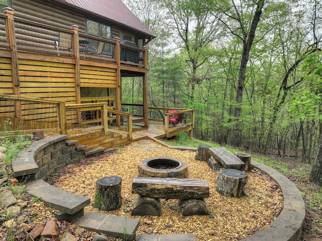 view of yard featuring an outdoor fire pit, a wooden deck, and a view of trees