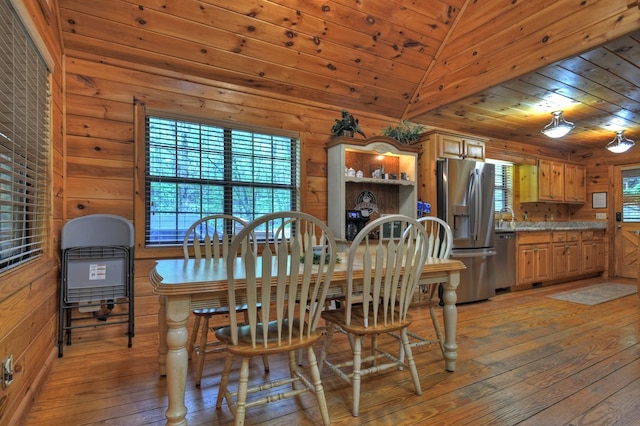 dining area with light wood finished floors, wooden ceiling, and wooden walls