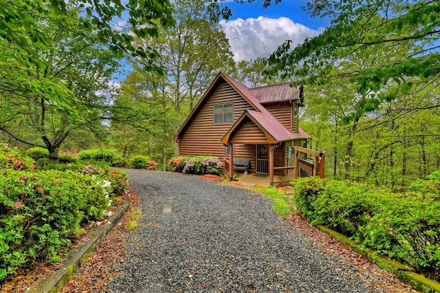 rustic home featuring driveway, metal roof, faux log siding, and a deck