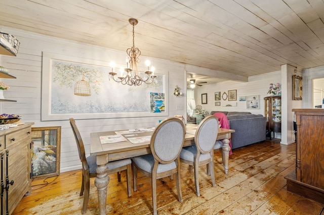 dining room featuring wood walls, ceiling fan with notable chandelier, wooden ceiling, and light hardwood / wood-style flooring