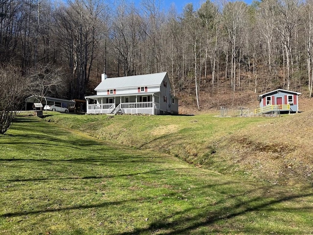 exterior space featuring a front lawn, covered porch, a chimney, a carport, and an outbuilding