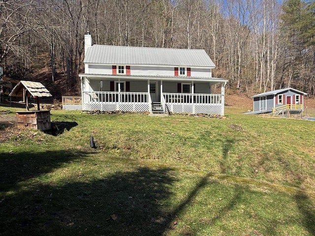 view of front of property featuring an outbuilding, a porch, a front yard, metal roof, and a chimney