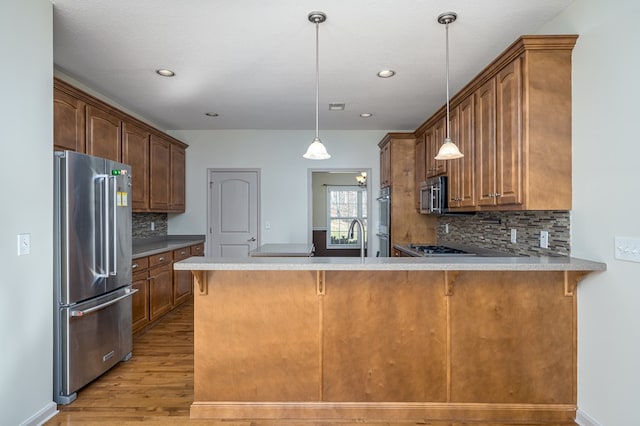 kitchen with stainless steel appliances, decorative light fixtures, decorative backsplash, and kitchen peninsula