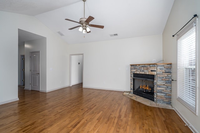 unfurnished living room with hardwood / wood-style flooring, vaulted ceiling, a stone fireplace, and ceiling fan