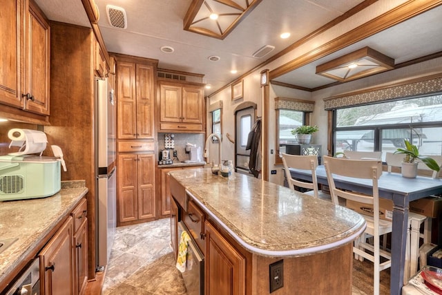 kitchen with stainless steel fridge, backsplash, ornamental molding, a center island, and light stone counters