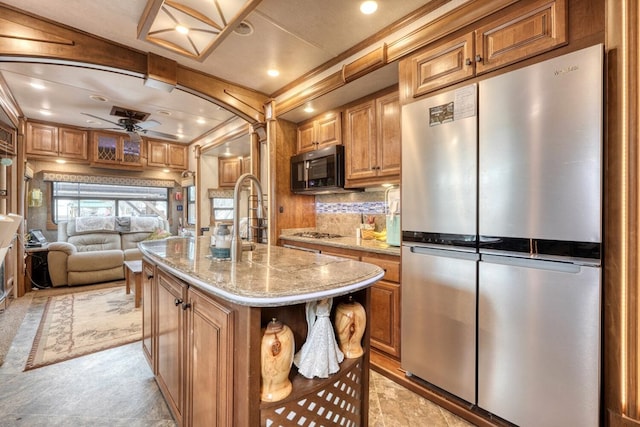 kitchen featuring backsplash, a kitchen island with sink, ceiling fan, stainless steel appliances, and light stone countertops