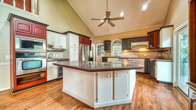 kitchen with light wood-style flooring, a kitchen island, glass insert cabinets, appliances with stainless steel finishes, and ventilation hood