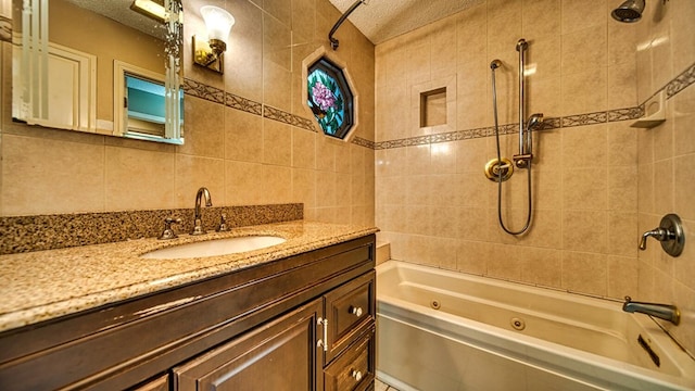 bathroom featuring a textured ceiling, a combined bath / shower with jetted tub, vanity, and tile walls