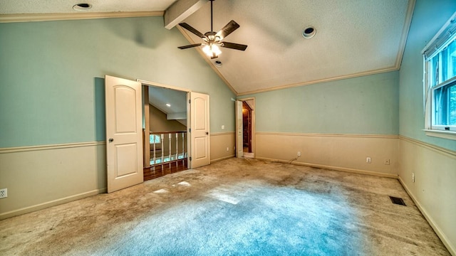 carpeted spare room featuring lofted ceiling with beams, a textured ceiling, visible vents, a ceiling fan, and ornamental molding