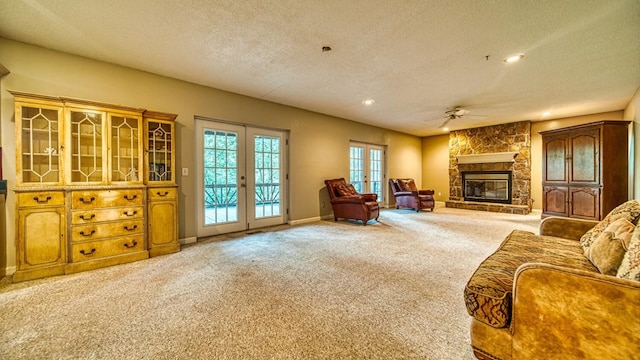 interior space featuring french doors, a ceiling fan, a stone fireplace, a textured ceiling, and baseboards