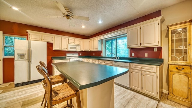 kitchen with light wood finished floors, white appliances, dark countertops, and a sink