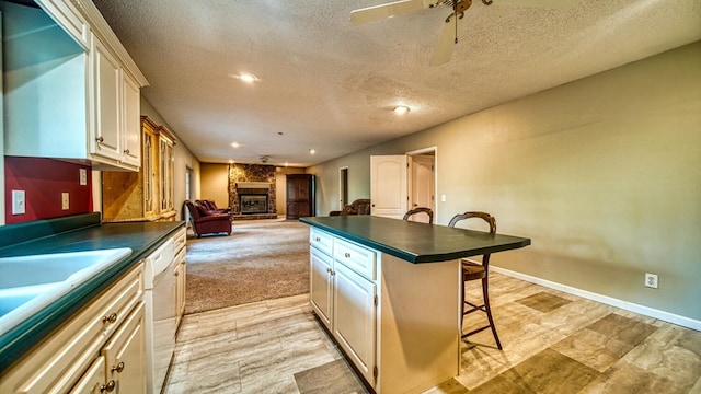 kitchen featuring dark countertops, a large fireplace, white dishwasher, and a breakfast bar area