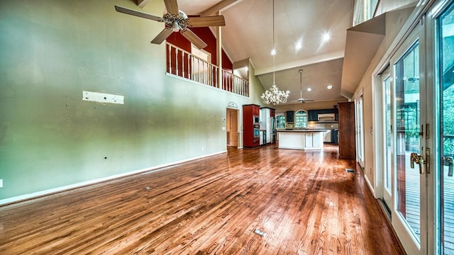 unfurnished living room featuring dark wood-style floors, baseboards, high vaulted ceiling, and ceiling fan with notable chandelier