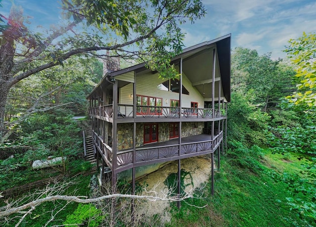 rear view of property featuring a deck, stone siding, and a chimney