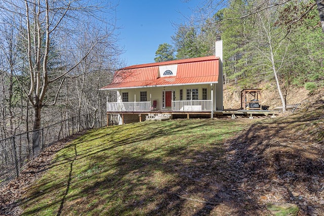 view of front facade with covered porch, a chimney, metal roof, and a front yard