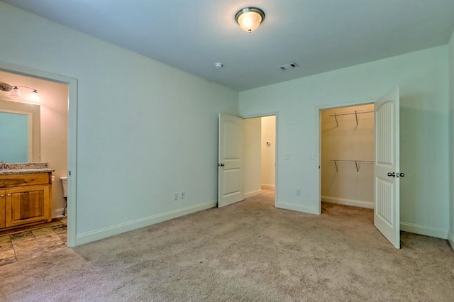 unfurnished bedroom with light carpet, connected bathroom, a spacious closet, and a closet