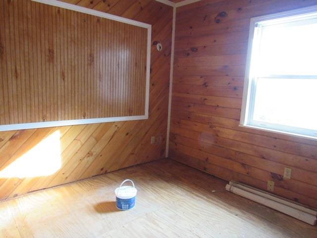 unfurnished room with a healthy amount of sunlight, wooden walls, and a baseboard radiator