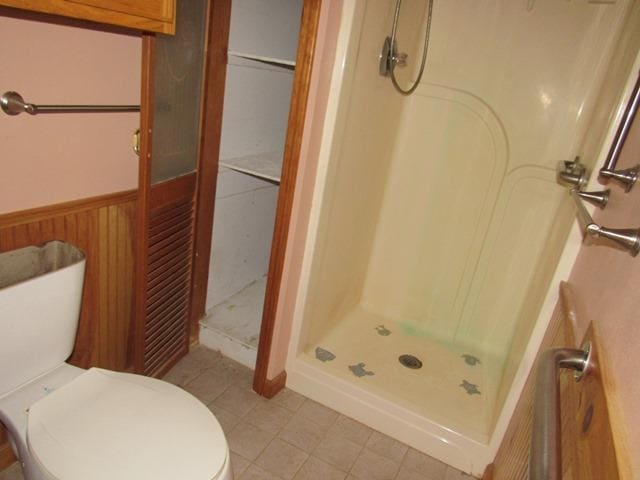 bathroom with a shower, toilet, and wood walls