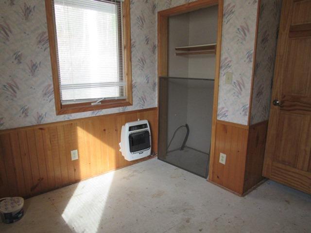 unfurnished bedroom with heating unit, wood walls, and multiple windows