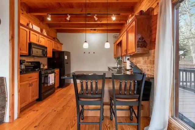 kitchen featuring beam ceiling, hanging light fixtures, rail lighting, black appliances, and light hardwood / wood-style floors