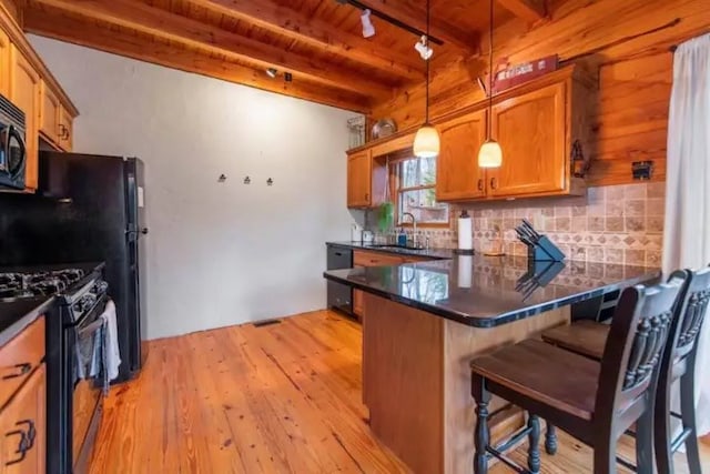 kitchen with hanging light fixtures, a kitchen breakfast bar, light hardwood / wood-style flooring, black appliances, and sink