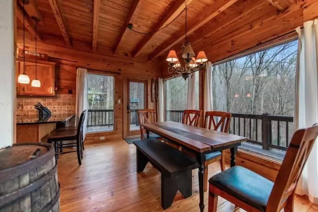 dining room with light hardwood / wood-style floors, wood walls, beam ceiling, and a wealth of natural light