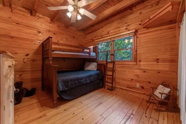 bedroom featuring beam ceiling, wood walls, light hardwood / wood-style flooring, and ceiling fan