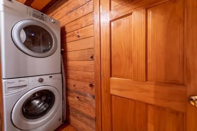 washroom with stacked washing maching and dryer and wooden walls