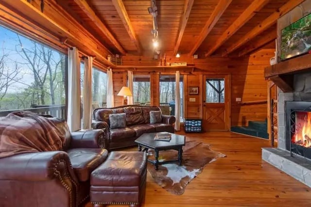 living room with a stone fireplace, beamed ceiling, wood-type flooring, and wooden walls