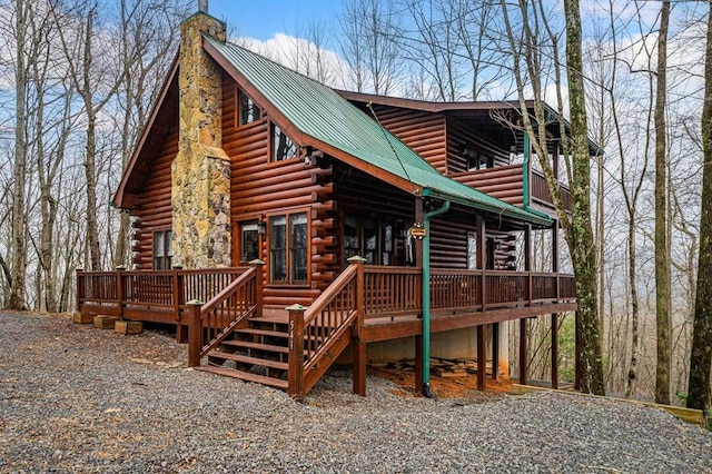 exterior space with a deck, log siding, metal roof, and a chimney