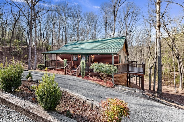 view of front of property featuring driveway, covered porch, metal roof, and a wooden deck