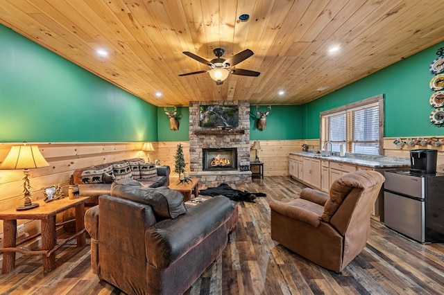 living room featuring a wainscoted wall, recessed lighting, a stone fireplace, wood finished floors, and wooden ceiling