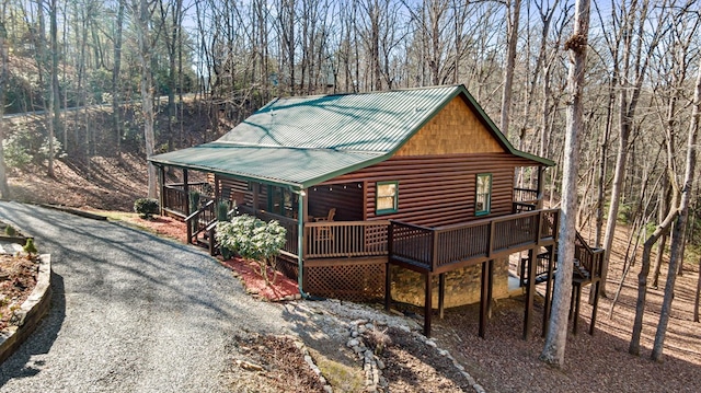 view of front facade featuring driveway, faux log siding, metal roof, and a wooden deck