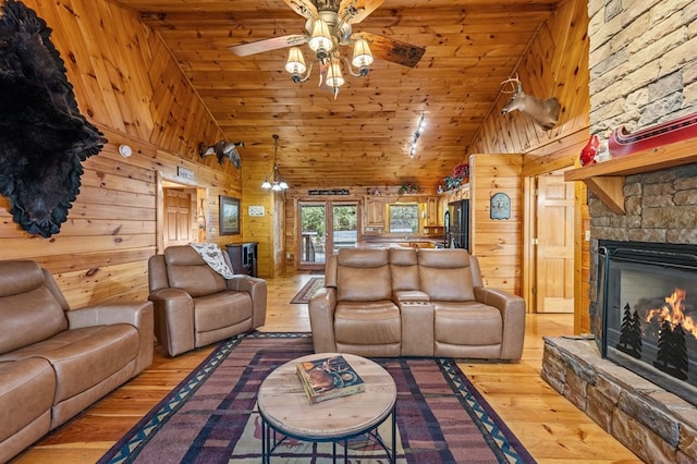 living area featuring high vaulted ceiling, light wood finished floors, wood walls, and a fireplace