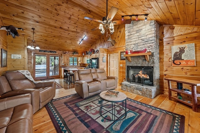 living room featuring a stone fireplace, light wood finished floors, wooden ceiling, and wooden walls