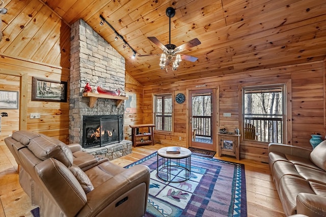 living room with wooden ceiling, ceiling fan, a stone fireplace, wood walls, and light wood-style floors