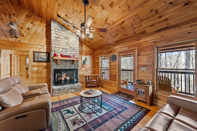 living room with lofted ceiling, a stone fireplace, wooden ceiling, light wood-style flooring, and wooden walls