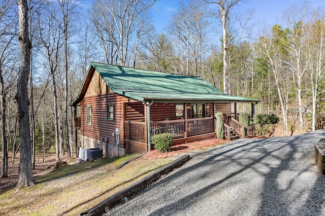 view of front facade with driveway, faux log siding, metal roof, a porch, and central AC