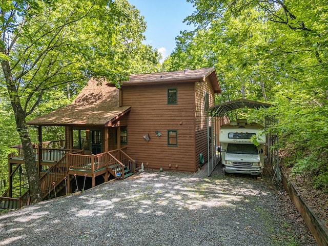 back of house with a detached carport, stairway, gravel driveway, roof with shingles, and a wooden deck