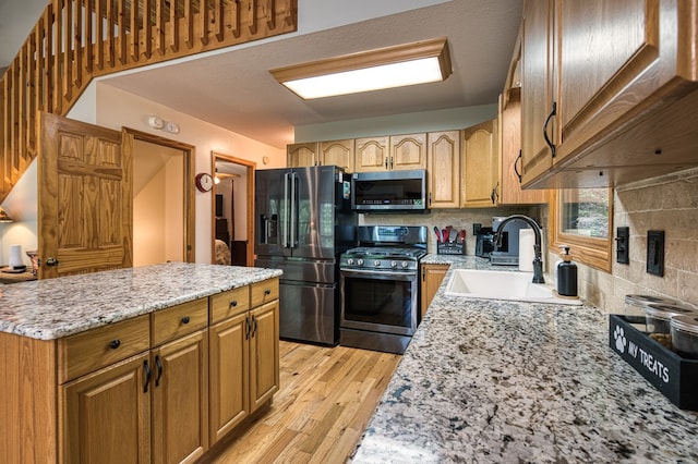 kitchen with stainless steel appliances, a sink, light wood finished floors, light stone countertops, and tasteful backsplash